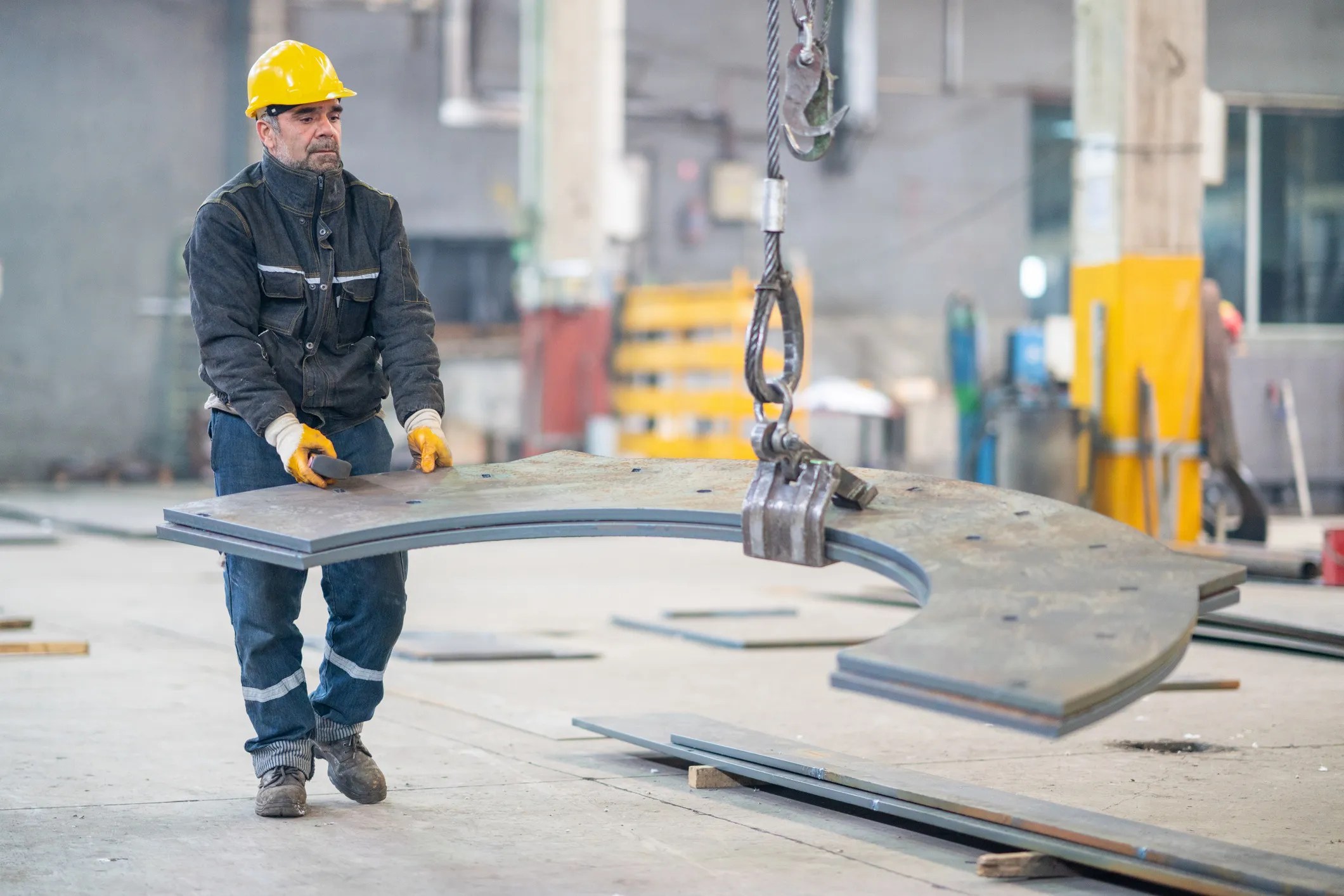 Senior worker holding and working with remote control for operating steel crane that adheres to ASTM A1001-18 high-strength steel castings for crane hooks, shackles, and heavy-duty lifting equipment.