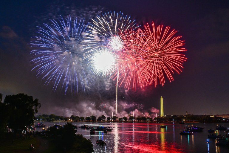 Fireworks illuminating the night sky above a lake filled with recreational boats during a Fourth of July celebration.