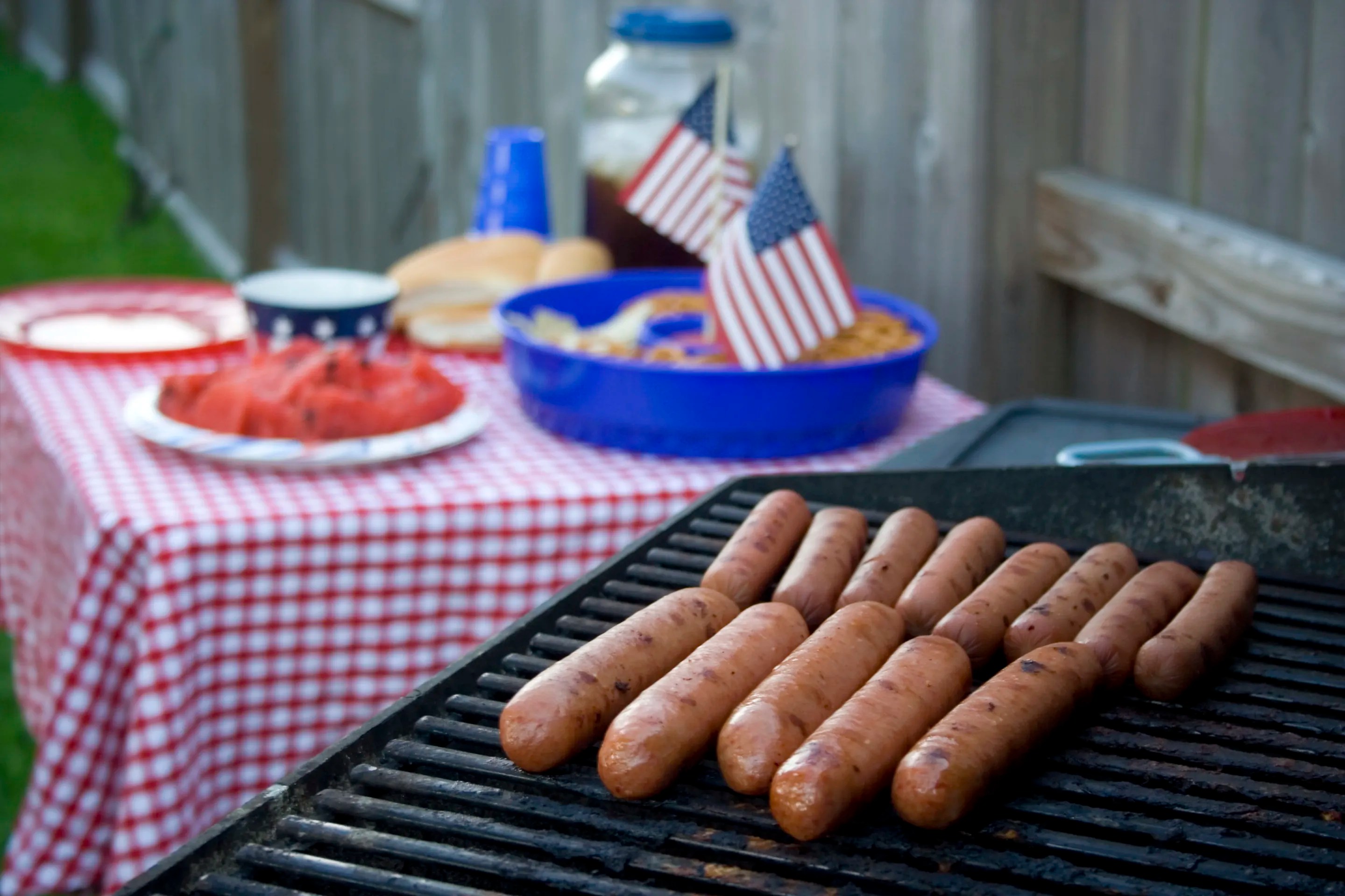 Family grilling burgers and hot dogs on a gas barbecue during a Fourth of July backyard cookout, highlighting outdoor grilling safety and product standards.