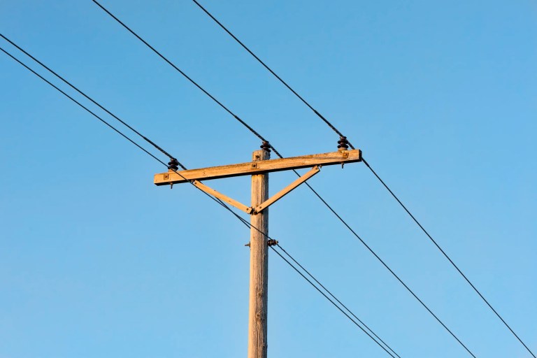 Wood utility pole with solid sawn wood crossarms supporting overhead power lines, illustrating ANSI O5.3-2021 specifications for electrical distribution infrastructure.