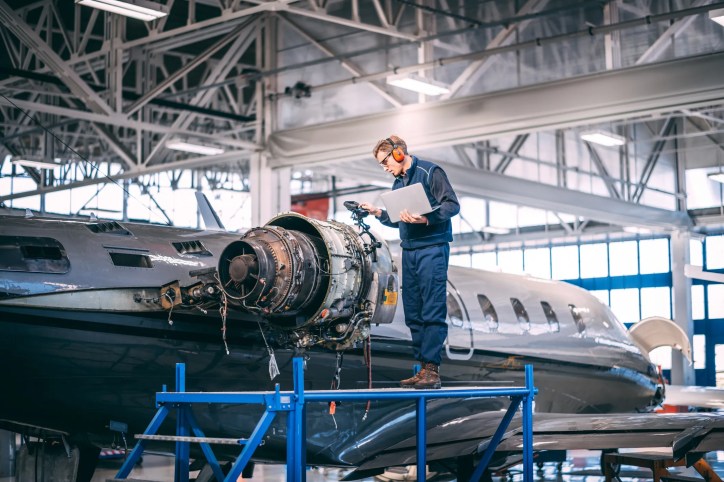 Engineer inspecting a commercial aircraft during manufacturing while technicians assemble aerospace components, illustrating AS9100 quality management and global aerospace supply chains.