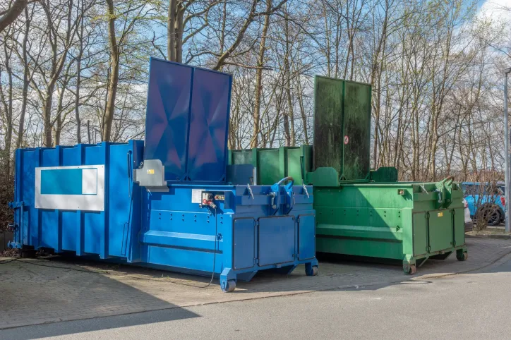 Stationary waste compactor, adhering to ANSI Z245.2-2026, installed outside a commercial building, compressing waste into a detachable container for efficient waste management.