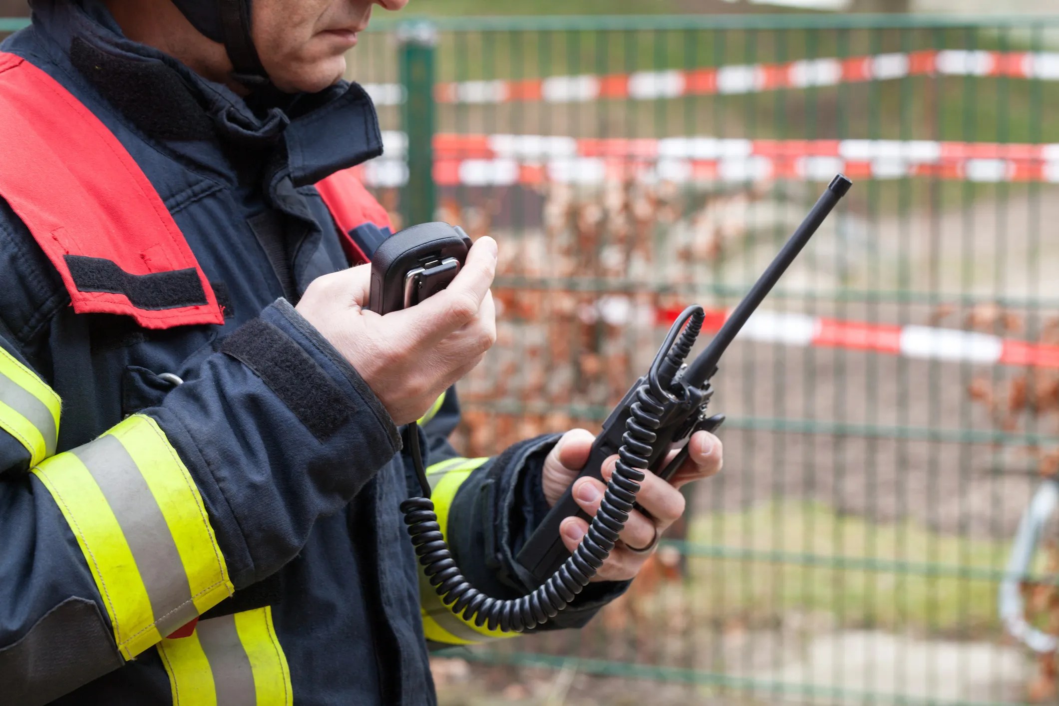 Firefighter using a handheld radio to communicate during an emergency response, illustrating Push-to-Talk over Cellular (PoC) communications, adhering to ATIS-0700016.