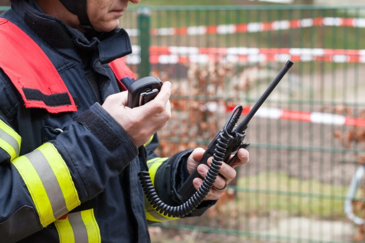 Firefighter using a handheld radio to communicate during an emergency response, illustrating Push-to-Talk over Cellular (PoC) communications, adhering to ATIS-0700016.