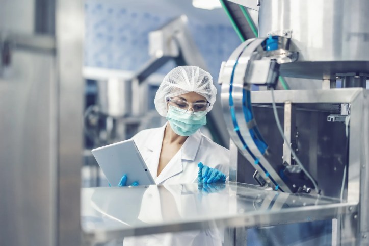 Assessor in mask and PPE working in accreditation by inspecting laboratory.