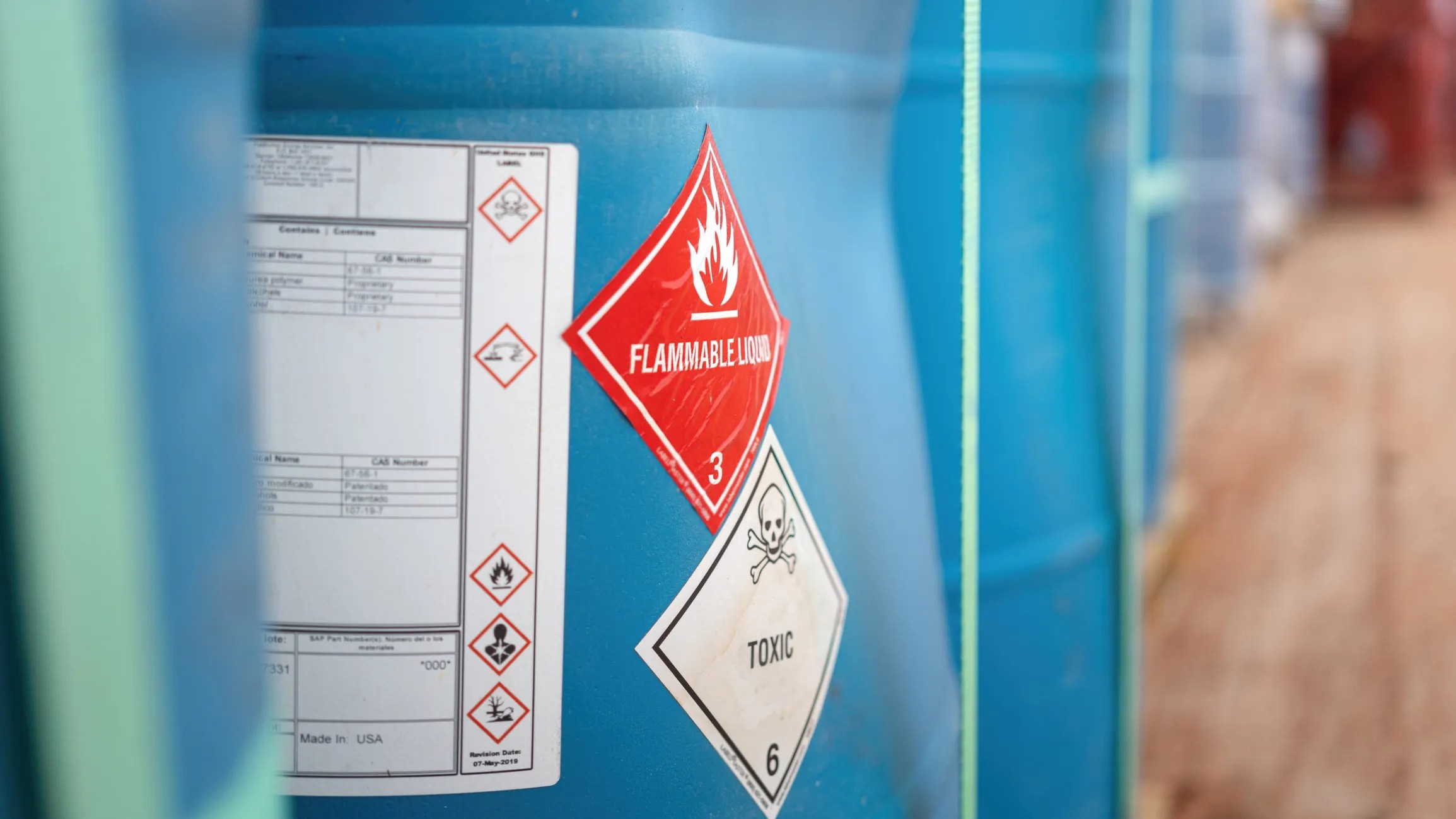 Flammable liquid and toxic hazard communication stickers on blue chemical container.